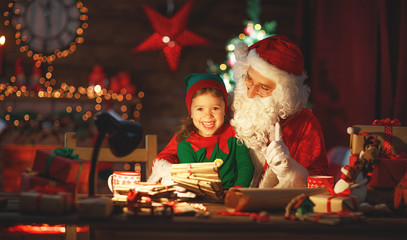 santa claus reads letter to little elf by Christmas tree