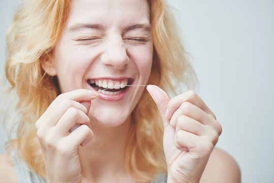 Young girl brushing her teeth with dental floss, close up on white background
