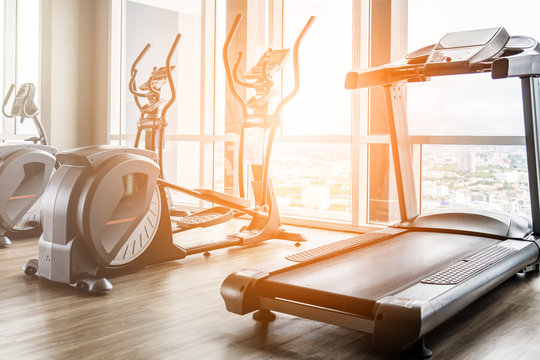 Fitness hall with elliptical and treadmill next to window with daylight morning. Exercise and health of city people at gym in the morning concept
