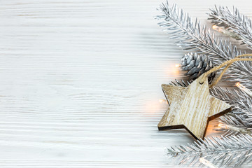 silver christmas tree branch with glowing garland and wooden star on white boards background