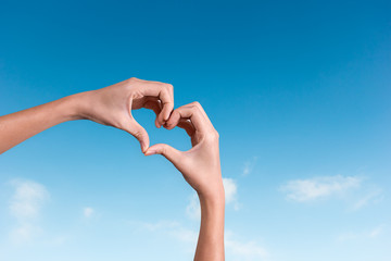 hands making a heart shape in the blue sky