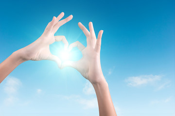 two hands making a heart shape in the blue sky