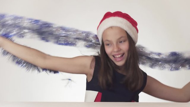 Beautiful teen girl in Santa Claus hat and New Year's tinsel happily and mischievously dances on white background stock footage video