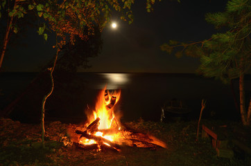 Big night bonfire on the riverbank in the forest clearing, flames, sparks and fireplace.