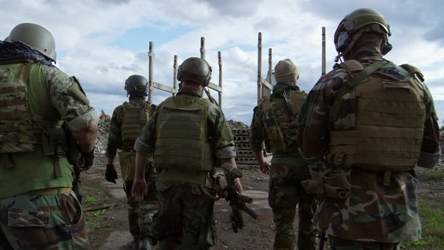 SLOWMO rear view of five soldiers armed with shotguns walking together in training area