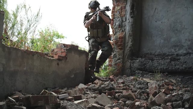 Tilt up handheld camera shot of military men walking one by one into destroyed building and aiming weapons