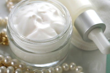 A jar of luxury beauty face cream and serum bottle with pearls teal mint aqua turquoise blue on color background with copy space. Styled feminine lifestyle image.
