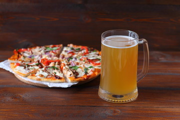 Mug of light beer and pizza with smoked meat and vegetables on dark wooden background.