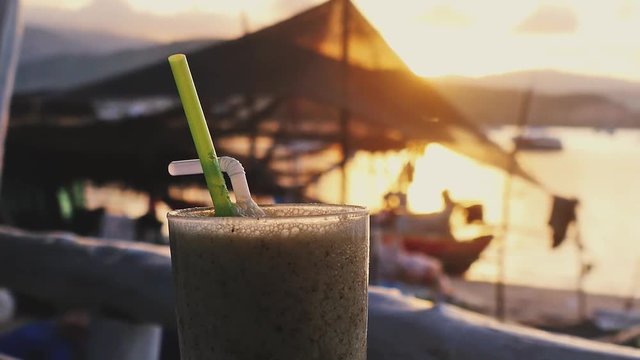 Glass of cocktail on the beach cafe at sunset time and boats in the sea. 1920x1080