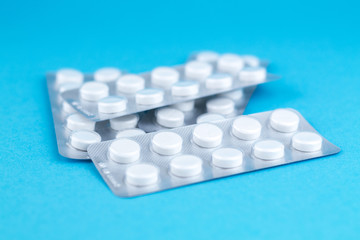 Packs of white pills packed in blisters with copy space on blue background. Focus on foreground, soft bokeh