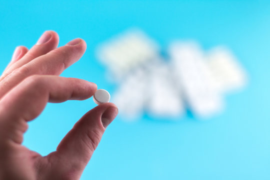 The man hand is holding a pill with copy space on blue background. Focus on foreground, soft bokeh