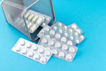 Trash bin with packs of white capsules and pills packed in blisters with copy space on blue background. Focus on foreground, soft bokeh