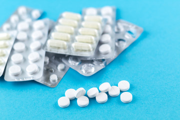 Full and empty packs of white capsules and pills packed in blisters with copy space on blue background. Focus on foreground, soft bokeh