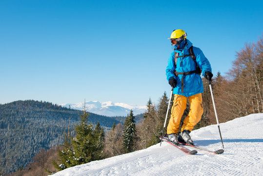 Shot of a professional skier in colorful gear skiing on fresh powder snow in the mountains on the winter resort. Blue sky and winter forest on the background