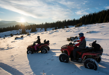 Young male and female riders sitting on quad bikes on snow, enjoying sunset in the the mountains in winter © anatoliy_gleb