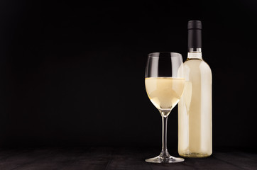 Bottle of white wine and wine glass mock up on elegant dark black wooden background, copy space.