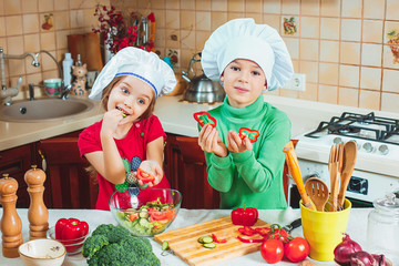 happy family funny kids are preparing the a fresh vegetable salad in the kitchen