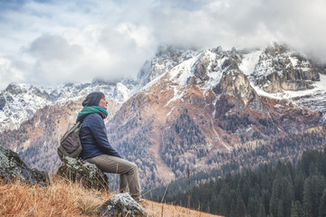 Young beautiful active traveler woman admiring the landscape sitting on a rock in the Dolomites, travel, lifestyle, vacations, unity with nature