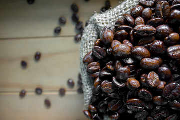 Roasted coffee beans in a small canvas bag - on a wooden table background.