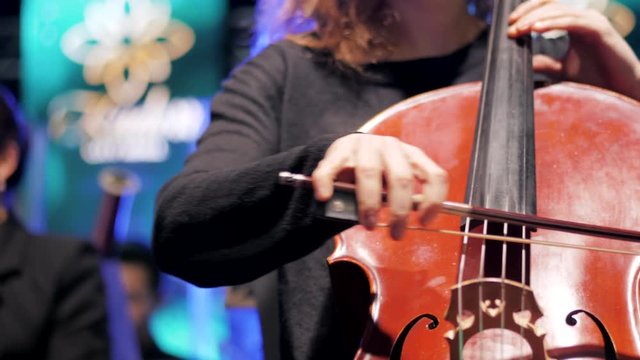 Close, full-frame detail on the hands, fingerboard and bowing technique of a professional cellist playing her instrument. 4k