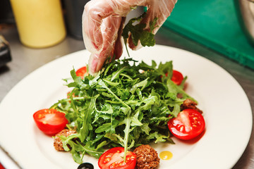 Cook prepares salad with arugula, cherry tomatoes and sauce