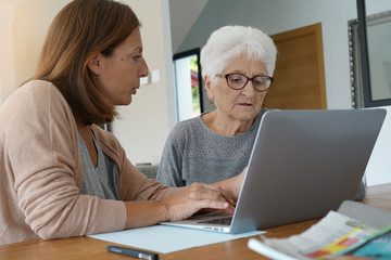 Fototapeta na wymiar Elderly woman using laptop with help of homecarer
