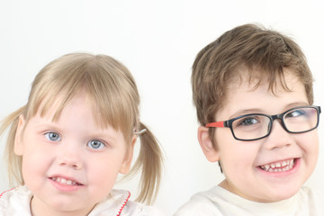 Happy little blonde girl and boy in glasses smiles in white studio