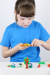 Beautiful girl molds toys from plasticine on white table in white room