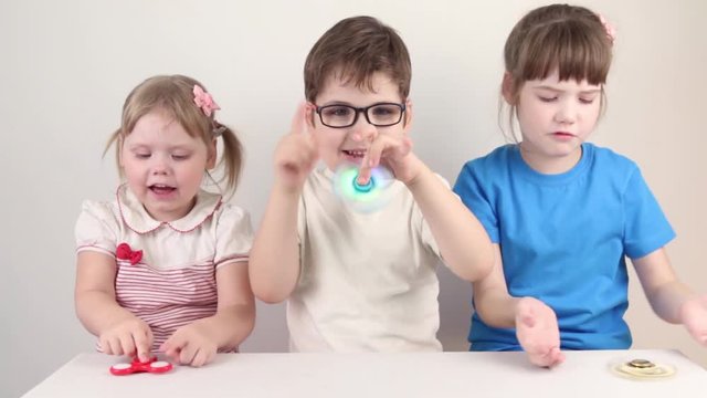 Three happy children play with spinners in white studio