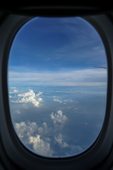Flying on the plane seeing sunrise light on abstract white cloud and shades of blue sky background with airplane wing through blurred window frame foreground