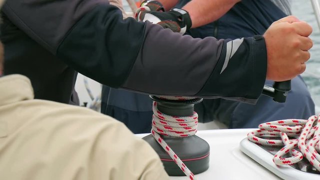 Sailing crew tightening up main sail winding rope through winch. Two of them pulling the rope and one turning winch handle. Filmed in slow motion hd.