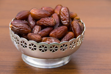 Dates fruit on a silver bowl on wooden table. The Muslim feast of the holy month of Ramadan Kareem