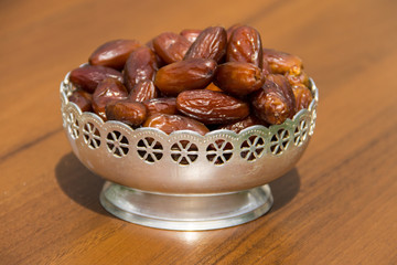 Dates fruit on a silver bowl on wooden table. The Muslim feast of the holy month of Ramadan Kareem