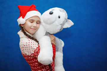 Little girl Santa celebrates Christmas with a toy dog Husky