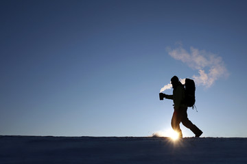 Man drinking hot coffee in thermos mug and looking into the mountains in snow, winter hike
