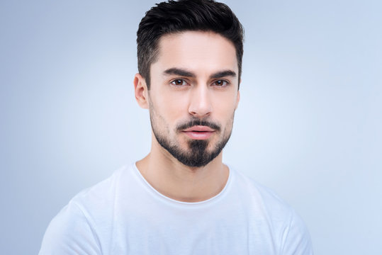 Calm. Bearded handsome young man looking calm and peaceful while standing against the blue background and looking straight