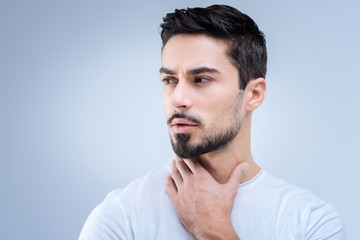 Fototapeta premium Strange feeling. Attentive serious young man looking worried about his health while standing and touching the neck with his fingers