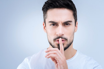 Quiet. Calm professional young teacher pressing his finger to the lips while asking his pupils to be quiet at the lesson