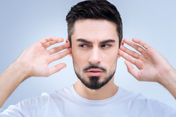 Unnecessary information. Stubborn clever young man looking aside while closing his ears with...
