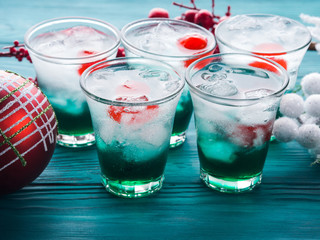 Christmas holiday party green alcohol drinks with cherry. Festive aperitif shots and ornaments on wooden dark table