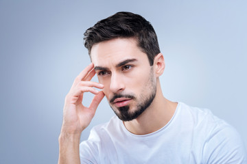 Fototapeta premium Concentrated worker. Clever hardworking experienced manager sitting with his fingers touching his head and thinking about the tasks for his new employees