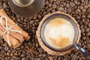 A cup of freshly brewed coffee, pot and cinnamon on coffee beans
