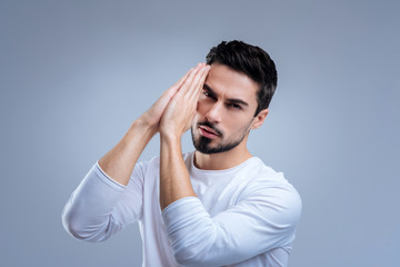 Not indifferent. Handsome calm young man feeling all spectrum of emotions while praying for the health of his relatives