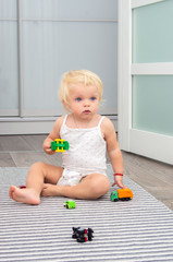 blond baby girl playing toy cars at home