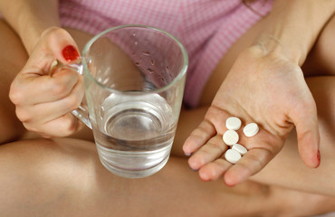 Girl holding a glass of water and pills. Closeup