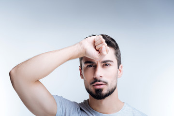 Obraz premium Strong muscles. Young handsome bearded sportsman standing against the blue background and looking thoughtful while showing his strong muscles