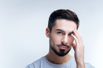 Obraz premium Uncomfortable. Tired ill young man standing against the blue background and touching his forehead while having a headache