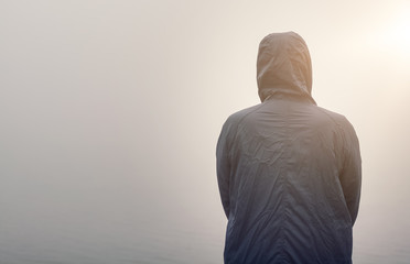 Ein anonymer Mann in Kapuzenjacke im Nebel Gegenlicht Rückansicht