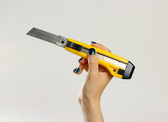 Female hands holding yellow sharp box cutter. Isolated on gray background. Closeup