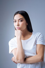 Thoughtful doctor. Calm responsible professional doctor standing against the blue background with her chin resting on the fist while looking attentively at the new patients